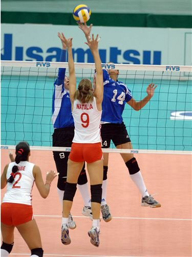 Una jugadora de voleibol env&iacute;a el bal&oacute;n al campo contrario mientras otras intentan un bloqueo.