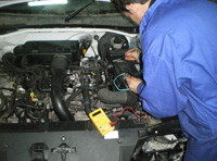 Lorenzo está con un polímetro en el cofre motor midiendo la tensión de la batería del vehículo.