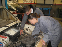 María y Lorenzo mirando el cofre motor de un vehículo.