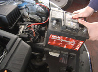 Técnico quitando una batería de un vehículo en taller.