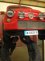 Lorenzo y maría revisando los bajos de un vehículo rojo.