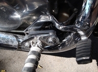 Fotografía de la parte inferior de una moto, en primer término se ve una estribera y el pedal del freno.