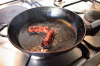 Foto de una sartén dónde se están friendo unas salchichas.