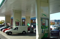 Foto de una gasolinera con los surtidores en primer plano y coches repostando.