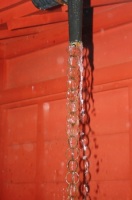 Foto de una cañería vaciando agua a chorro en posición vertical sobre fondo rojo.