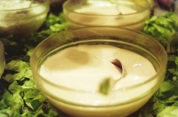 Se observa un recipiente de cristal con mayonesa casera sobre un lecho de hojas de lechuga.