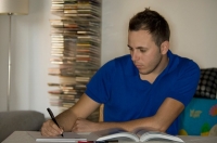 En este caso, Juan está en el interior de su vivienda, sentado. Frente a él, una mesa con un libro y un cuaderno en el que toma nota.