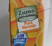Podemos ver un envase de zumo de naranja en primer plano donde se ha resaltado la leyenda “Rico en vitamina C” y se señala el carácter 100 % natural.