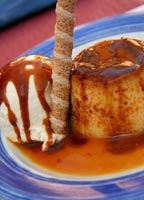 Podemos ver un flan tamaño individual con una bola de helado, ambos decorados con caramelo líquido, de color marrón intenso.