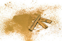 Se ven una ramas de canela al lado de un montoncito de canela en polvo.