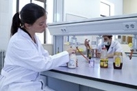 Podemos ver una chica con bata blanca, sentada en una mesa de laboratoito inspeccionando unos botes con diversas sustancias.