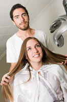 Imagen de una chica sentada cogiéndose el cabello con las manos mientras detrás hay un chico con camisa blanca.