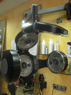 Se ve un aparato negro con placas metálicas circulares. Tres de ellas forman el cuerpo del aparato y dos en los laterales le dan el aspecto de brazos. Está sujeto a la pared por un brazo articulado.