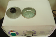 Aparato blanco con un hueco destapado en la parte superior donde se alojan unas bolitas transparentes llamadas perlinas. Tiene en el frente un interruptor y un regulador.