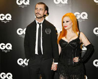  Imagen de la cantante Alaska que posa de la mano de un caballero, delante de un telón negro con letras