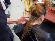 Imagen de una chica de cabello largo, protegida con una capa negra y una profesional haciendole unas mechas con peine.