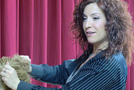 Imagen de una chica sobre un escenario con telón morado, manipulando el cabello de una persona rubia.