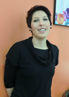  Imagen de una chica morena de cabello corto, con una blusa negra, ligeramente apoyada  en la pared.