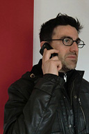  Imagen de un chico con gafas,moreno, con chaqueta negra, que habla por teléfono.