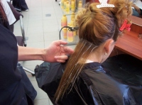 Imagen de una clienta de cabello largo a quien le están realizando unas mechas con peine. Se ve el cabello de color con una líneas blancas donde ya se ha puesto el decolorante.