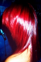 Imagen de un cabello rojizo y violeta, en colores muy intensos de fantasía. La imagen está tomada por la parte posterior, pero se ve también el lateral. En el fondo, la pared es de color azul.