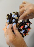 Cabeza de maniquí con bigudíes puestos y unas manos con algodones limpiando el líquido que toca el cuero cabelludo.