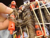 Se observa un cabello enrollado con bigudies y una mano del profesional desenrollando un bigudí y comprobando su rizo.