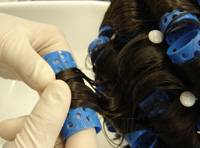 Cabeza montada con rulos y profesional de la peluquería desenrollando un rulo para comprobar el rizo.