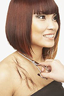 En la imagen se ve a una modelo sonriendo, con el cabello castaño rojizo, lleva el cabello cortado sólido sobre los hombros, le están terminando el contorno del corte de cabello.
