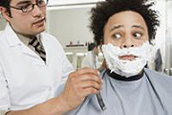En la imagen se ve Un barbero dispuesto a afeitar a un cliente, el rostro del cliente refleja miedo hacia algo que lleva en la mano.