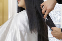 Técnica desfilado. Se ve una usuaria con el cabello largo y oscuro. Una mano que sujeta una tijera de filos rectos, le está realizando la técnica de desfilado en la zona de medios.