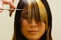 Se ve una modelo con el cabello de la zona frontal sobre el rostro. Unas manos accionan una tijera para cortarlo (I).
