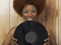 Se ve una chica con el cabello rizado, cortado en redondo, sujeta con las manos un disco de vinilo, frente a su rostro.