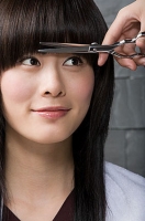 Se ve una modelo con el cabello de la zona frontal sobre el rostro. Unas manos accionan una tijera para cortarlo.