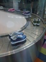 Cinta trnsportadora de metal moviendose con pares de zapatillas sobre ella.