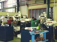 Máquinas industriales de un taller en el que se ven varias personas trabajando en distintas maquinas automaticas y semiautomaticas.