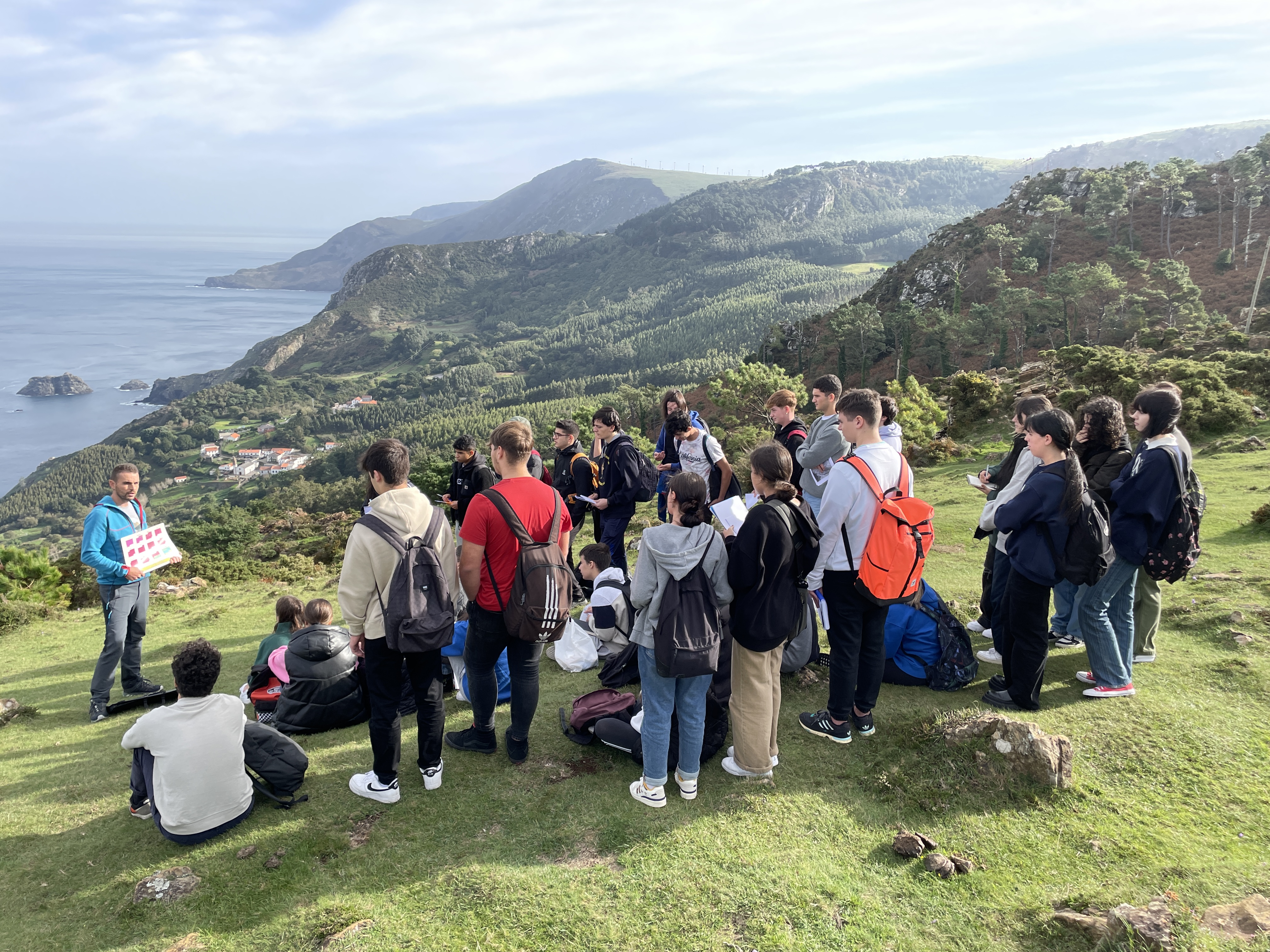 Fran canosa explicando a xeoloxía de Santo Andrea de teixido ante o alumnado e Santo Andrea ao fondo.
